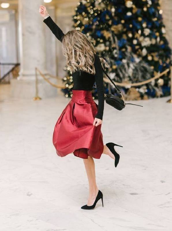 un col roulé noir, une jupe rouge foncé en ligne A, des talons noirs et un sac pour une tenue de Noël élégante qui ne nécessite pas d'achats